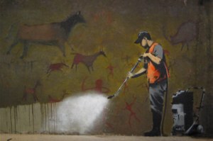 A wall with pictures like the cave art of Lascaux, and a council worker removing the graffiti with a steam cleaner.